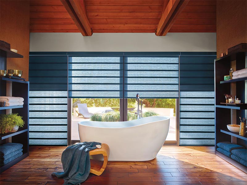 Modern bathroom with freestanding tub and layered window shades.