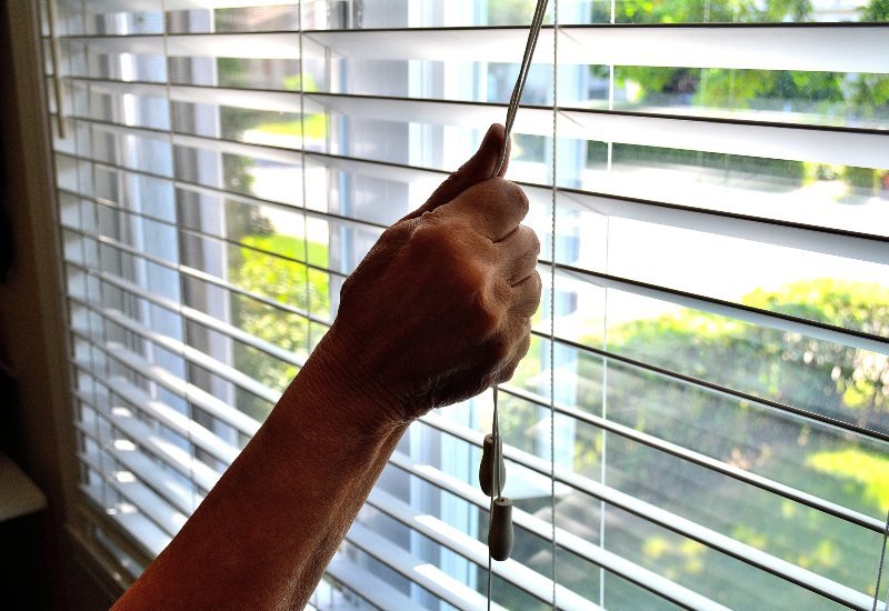 An Individual showcasing composite window blinds with cords for practical use in Tucson, AZ.
