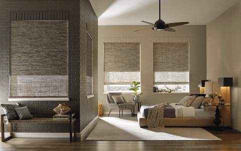 Woven wood shades cover a window in a cozy bedroom featuring a bed and a chair in Tucson, AZ.