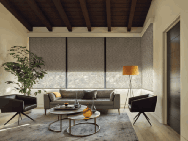 Custom roller shade in a living room with a couch, table, lamp, & a large window in Tucson, AZ.